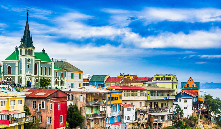 Bunte Häuser und eine grüne Kirche mit Turm stehen unter blauem Wolkenhimmel