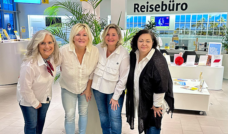 Vier Frauen mit freundlichem Gesichtsausdruck stehen lächelnd im Reisebüro zusammen