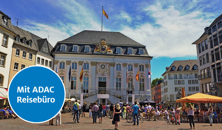 Ein belebter Platz mit einem historischen weißen Gebäude bei klarem Himmel.