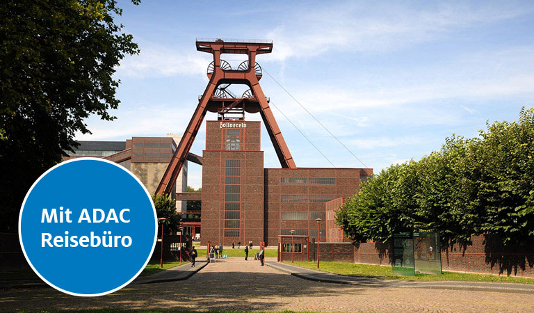 Historischer Bergbaukomplex mit Backsteinfassaden und grünem Baumensemble.