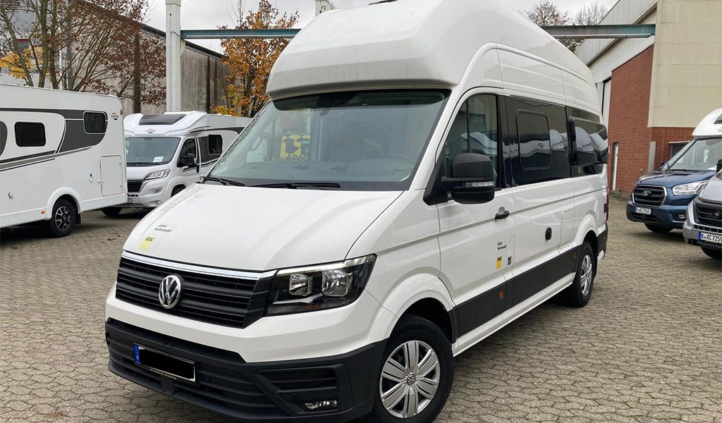 Ein weißer VW Kastenwagen mit Hochdach steht auf einem gepflasterten Hof