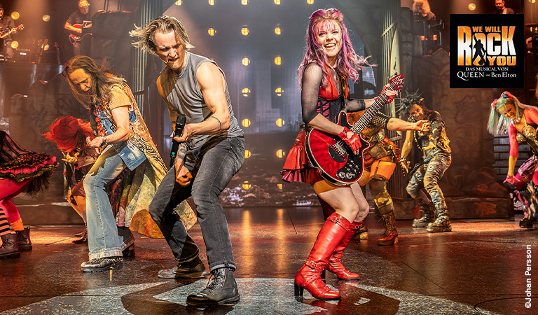 Mehrere Musiker mit rockigen Outfits und energiegeladenen Gesichtsausdrücken auf Bühne