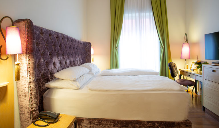 Helles Schlafzimmer mit großem violetten Bett, grünen Vorhängen und modernen Lampen