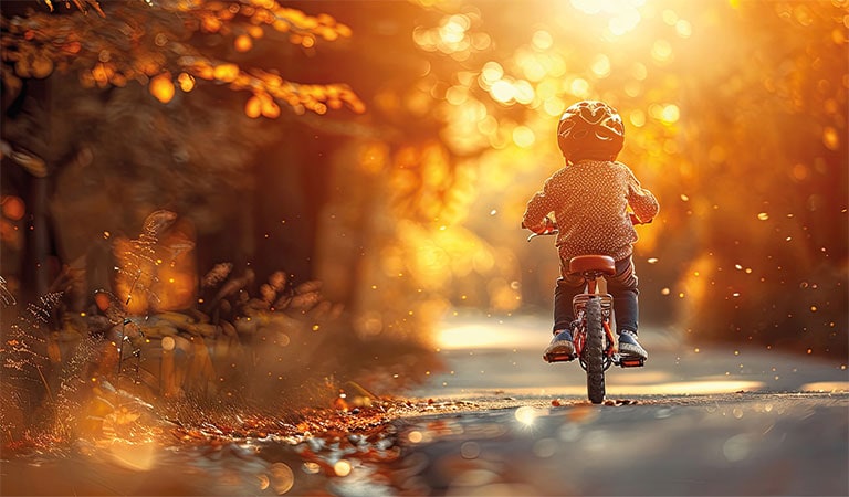 Kind auf Fahrrad im Herbstwald, Sonnenuntergang, Blätter fallen, Helm tragend, warmes Licht.
