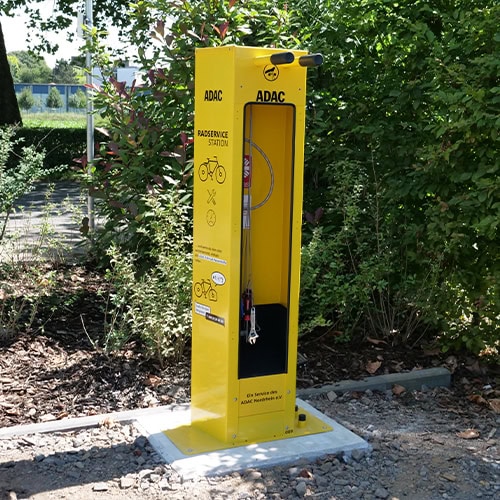Gelbe ADAC-Fahrradservicestation im Freien mit Werkzeugen; Schilder und Anleitungen auf der Station.