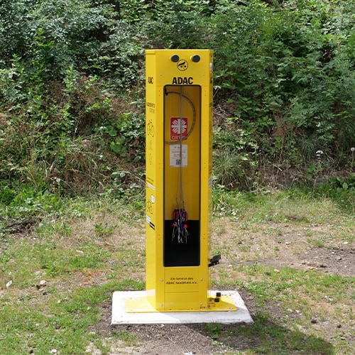 Ein gelbe ADAC-Fahrrad-Servicestation im Grünen mit Werkzeugen, aufrecht stehend.