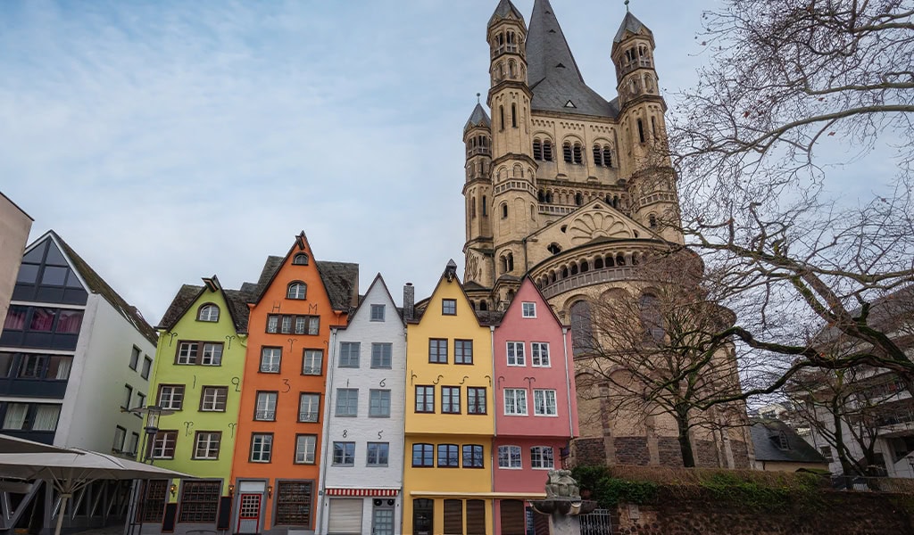 Bunte historische Gebäude vor einer großen Kirche, bewölkter Himmel, keine Personen sichtbar.