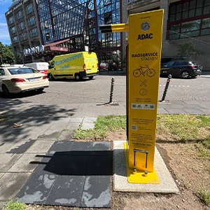 ADAC-Fahrradstation auf Gehweg in Stadt, gelb, mit Luftpumpe und Werkzeug; sonniger Tag.