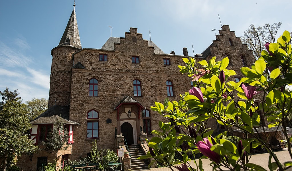 Eine mittelalterliche Burg mit Zinnen, umgeben von blühenden Bäumen, unter klarem Himmel.