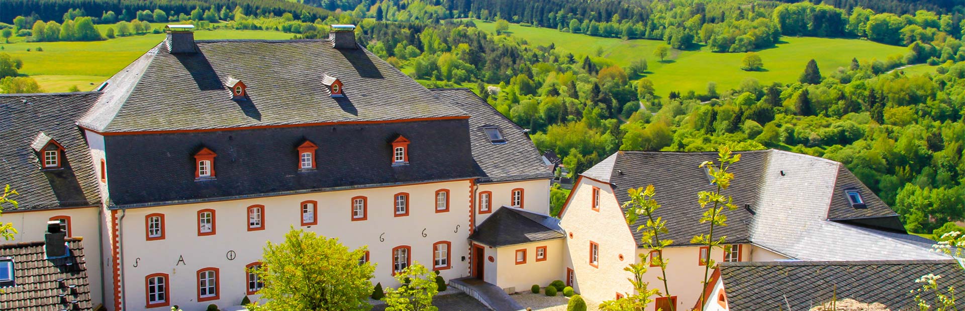 Luftaufnahme eines malerischen, weißen Klosters mit Schieferdach in grüner Landschaft.