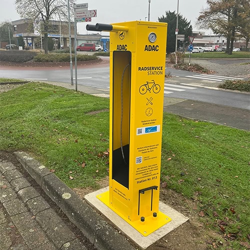 Gelbe ADAC-Radservice-Station mit Pumpe, blauer Bedienungsanleitung und grünem Rasen im Hintergrund.