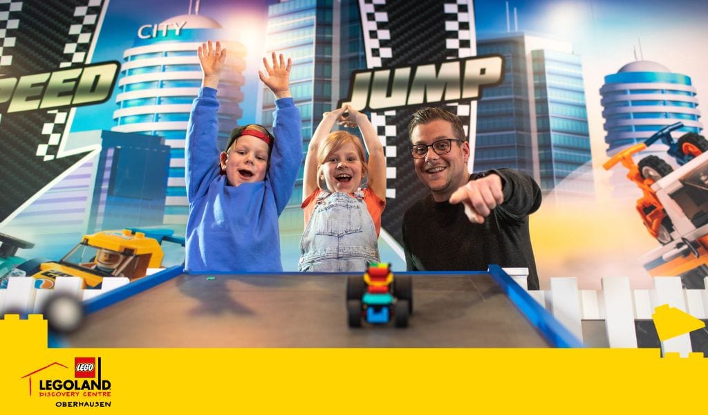 Ein Mann und zwei Kinder jubeln bei einem LEGO-Spiel im LEGOLAND Discovery Centre Oberhausen.