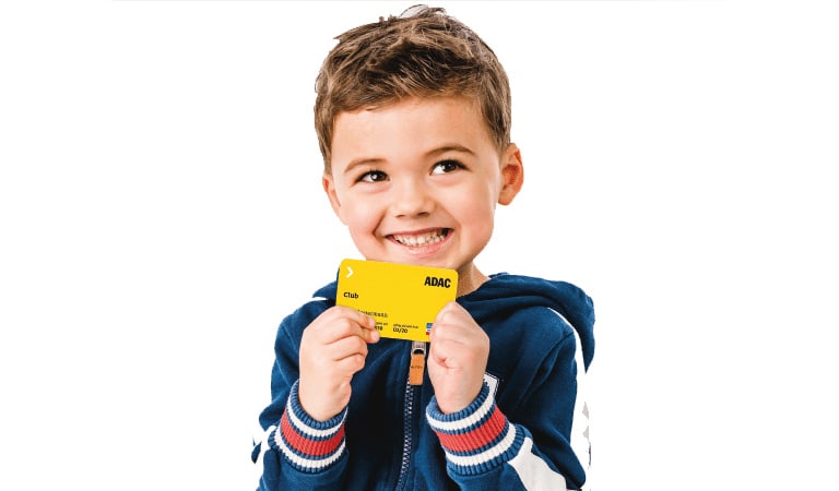 Junge lächelt freudig, hält gelbe Karte mit ADAC-Logo, trägt blau-weißen Hoodie.