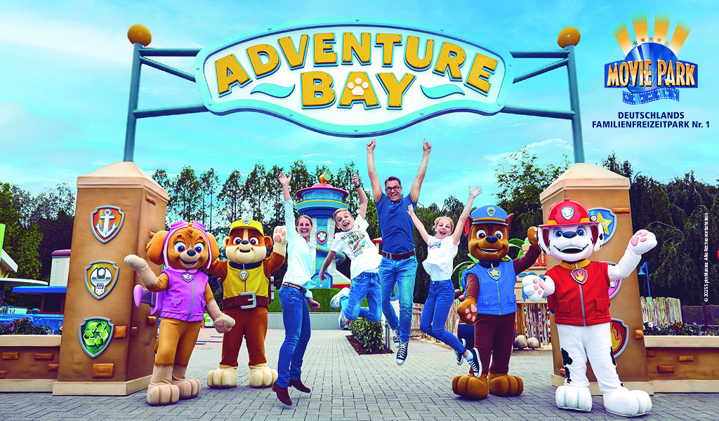 Fünf Personen springen freudig vor dem "Adventure Bay"-Eingang mit Maskottchen in bunten Kostümen.