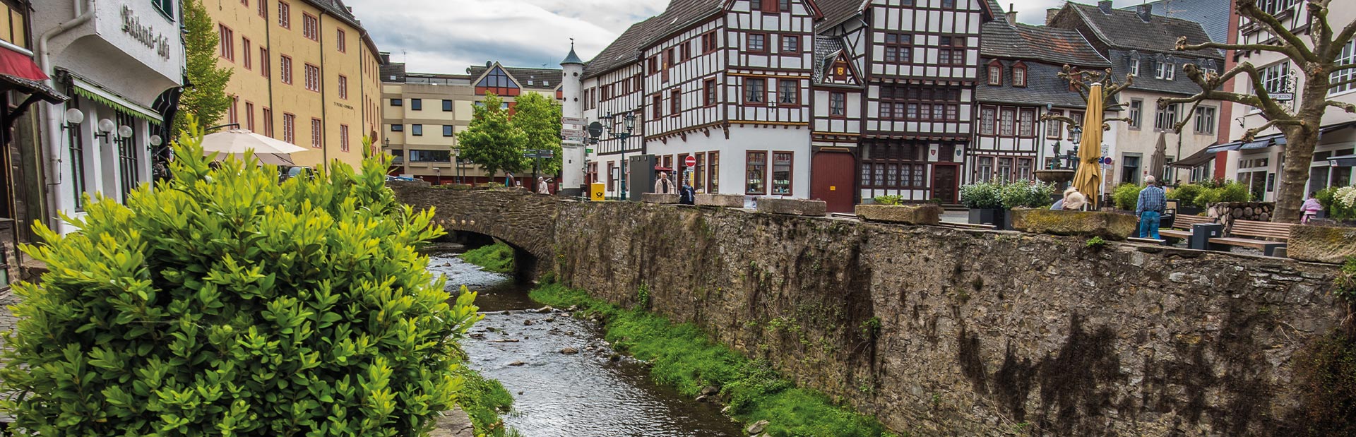 Eine malerische Altstadt mit Fachwerkhäusern, einem Bach und einer steinernen Brücke.