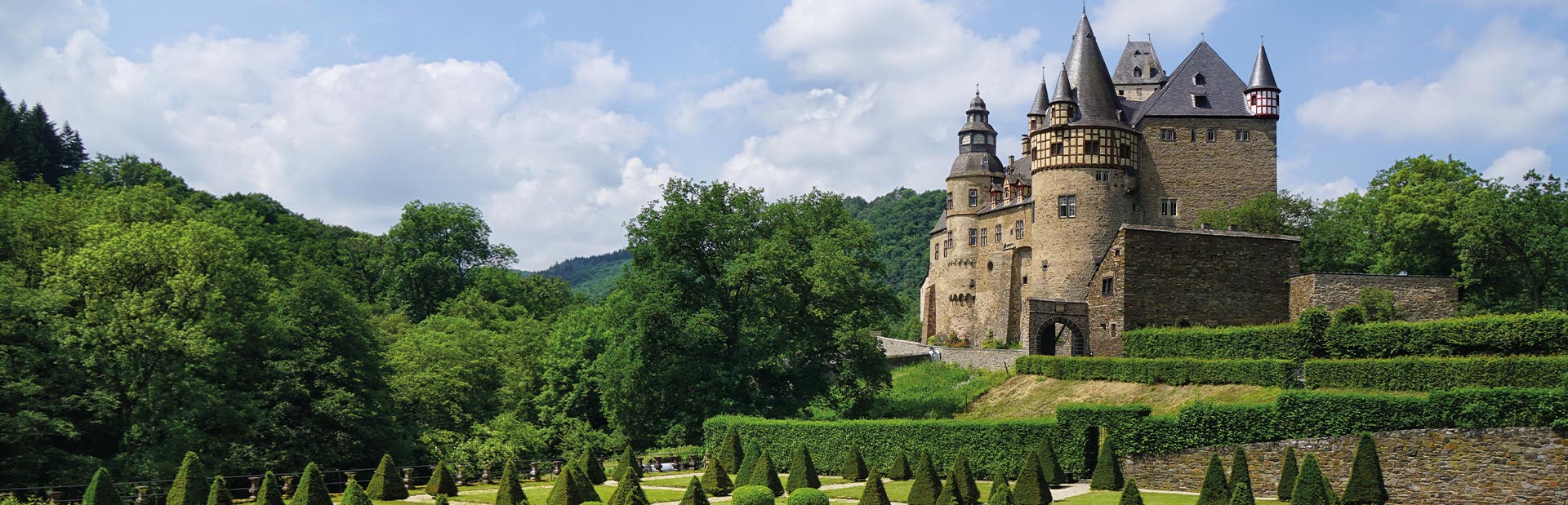Ein historisches Schloss aus Stein mit Türmen, umgeben von üppiger grüner Vegetation.