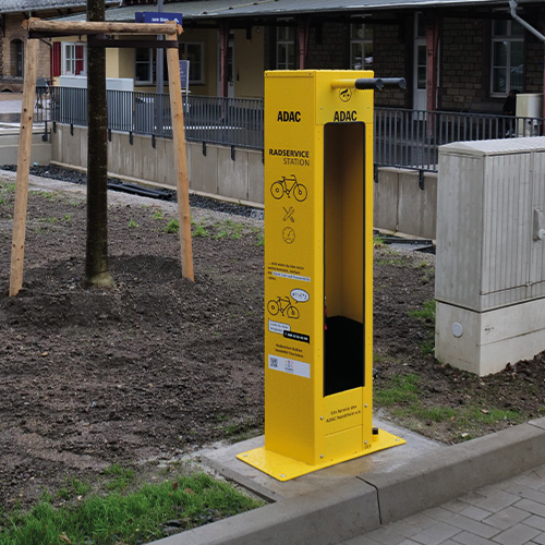 Gelbe ADAC-Radservicestation neben einem Baum, mit Werkzeugen zur Fahrradreparatur.