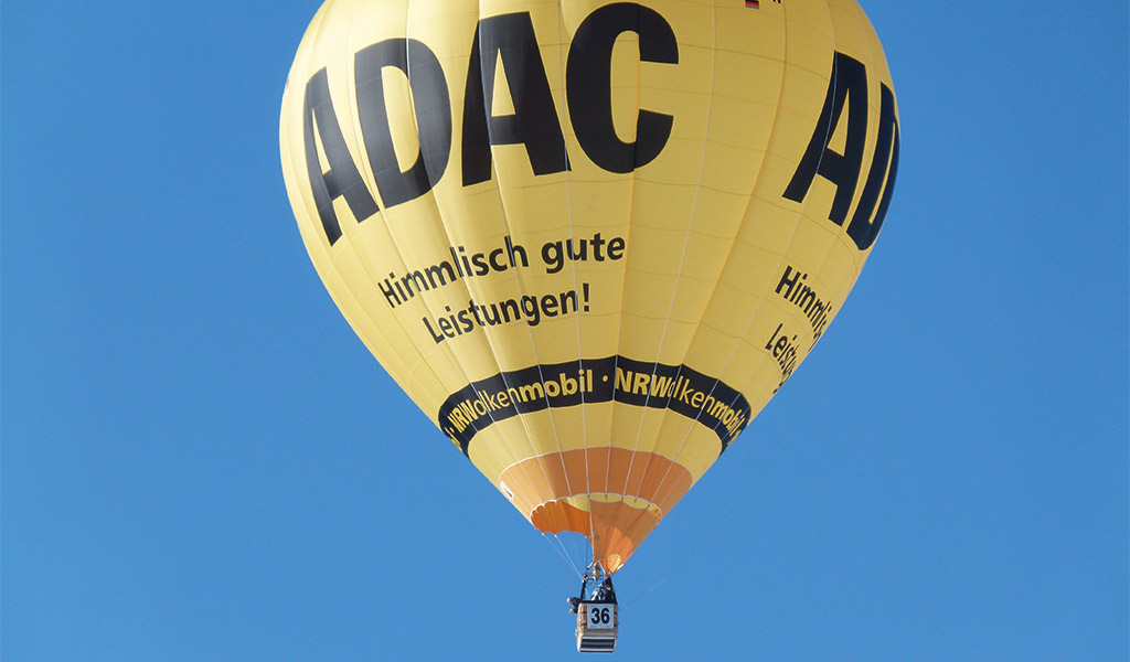 Gelber Heißluftballon mit ADAC-Logo am blauen Himmel, Korb ist menschenleer.
