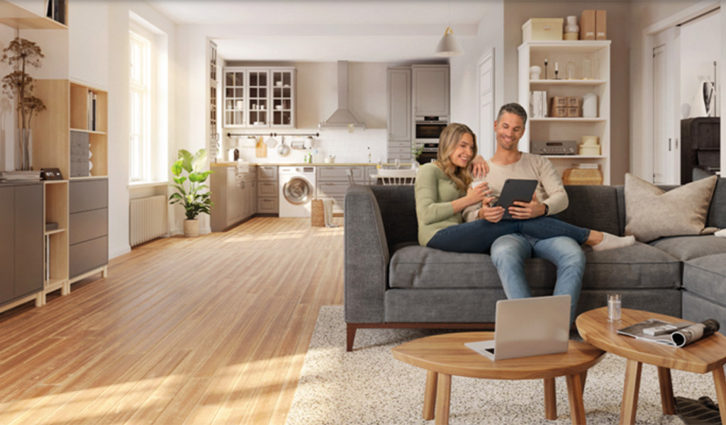 Ein lächelndes Paar sitzt auf einem grauen Sofa in einem modernen Wohnzimmer mit Holzboden.