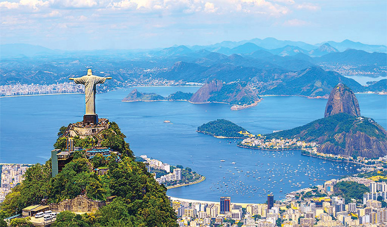 Luftaufnahme von Rio de Janeiro mit Christusstatue, blauen Bergen und belebter Stadt im Vordergrund.