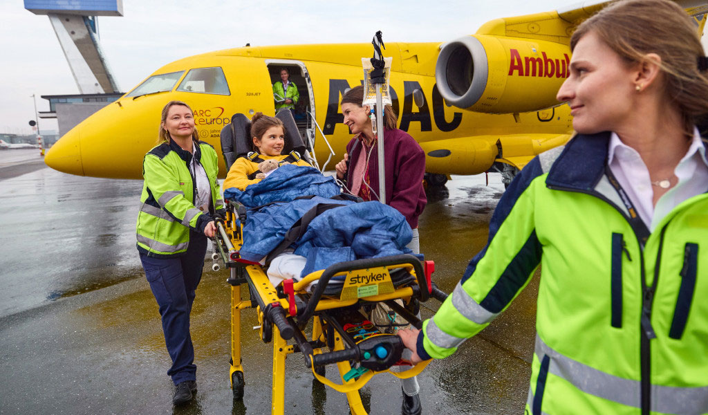 Eine Person auf einer Trage vor einem gelben ADAC-Hubschrauber, mit medizinischem Team.