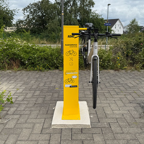 Fahrrad steht an einer gelben Radservicestation auf grauem Pflasterweg.