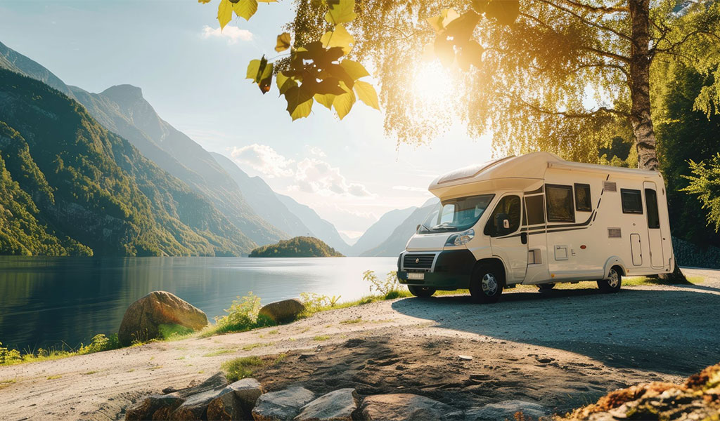 Ein weißes Wohnmobil steht idyllisch am See unter einem sonnigen Himmel.