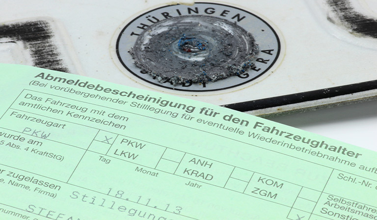 Ein grünes Formular liegt vor einem abgenutzten Kfz-Kennzeichen aus Thüringen.