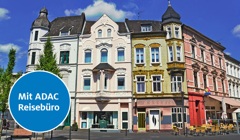 Drei bunte Altbauten mit dekorativen Fassaden vor blauem Himmel.