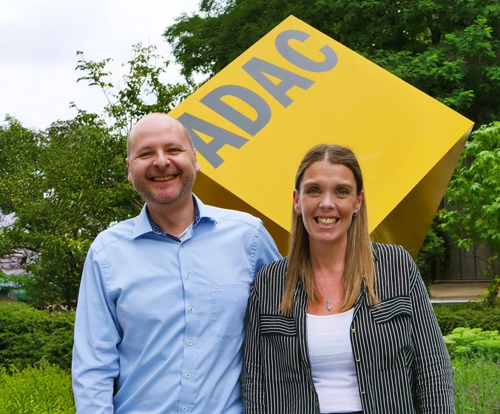 Zwei lächelnde Personen stehen vor einem großen gelben ADAC Würfel im Grünen