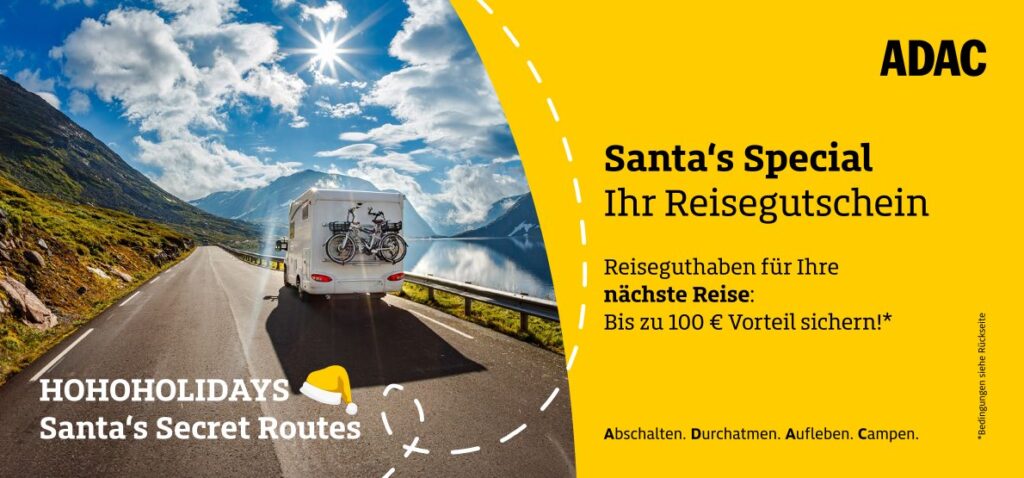 Ein Wohnmobil fährt auf einer sonnigen Landstraße an einem See entlang, Berge im Hintergrund