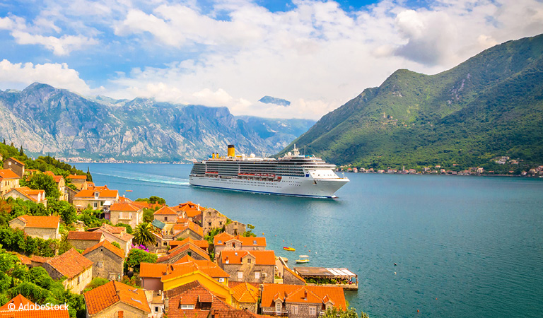 Sonnige Küstenstadt mit weißen Gebäuden auf Klippen, blauem Meer und lila Blumen im Vordergrund.