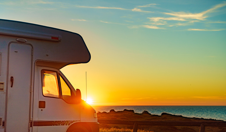 Ein weißes Wohnmobil steht bei Sonnenuntergang am Meer, der Himmel ist orangeblau