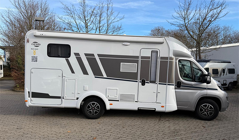 Ein weiß-graues Wohnmobil steht seitlich auf einem Parkplatz mit blauen Himmel