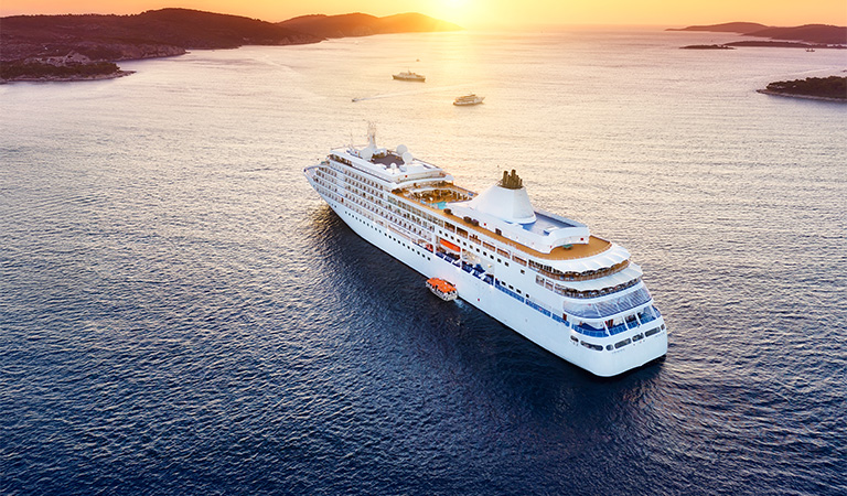 Ein großes weißes Kreuzfahrtschiff fährt bei Sonnenuntergang durch ruhiges blaues Meer