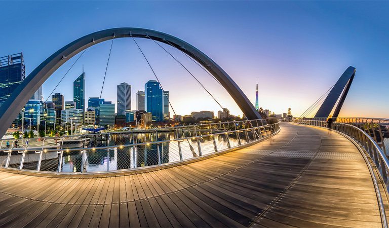 Eine moderne Fußgängerbrücke mit geschwungenen Bögen bei Sonnenaufgang über dem Wasser