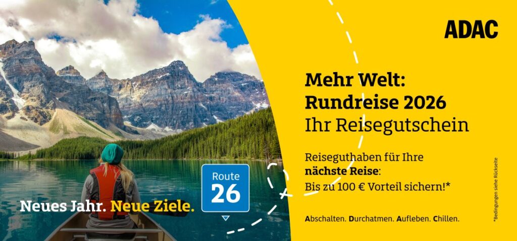 Eine Person im roten Mantel blickt entspannt auf einen türkisfarbenen Bergsee vor Bergen