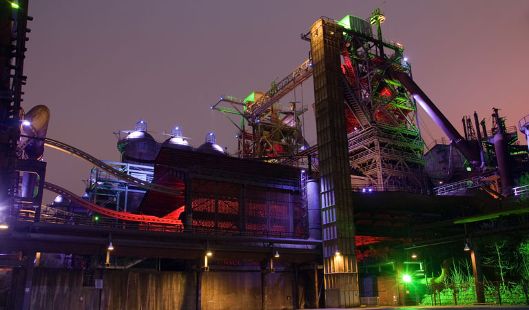 Eine bunt beleuchtete Industrieanlage strahlt nachts mit grünen und roten Lichtern