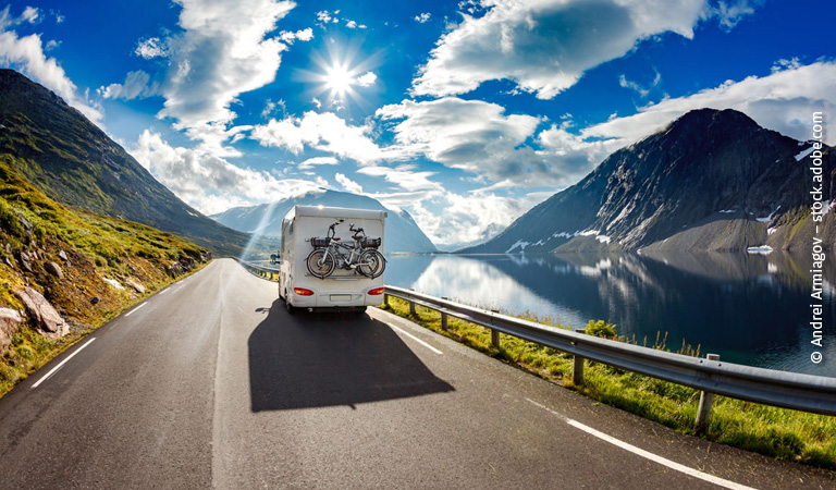 Ein weißes Wohnmobil mit Fahrrädern fährt auf einer Straße am malerischen See entlang