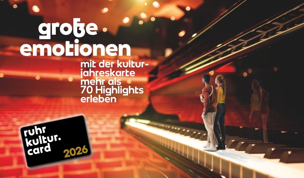 Zwei Personen stehen eng beieinander auf einer Klaviertastatur vor leerem Konzertsaal