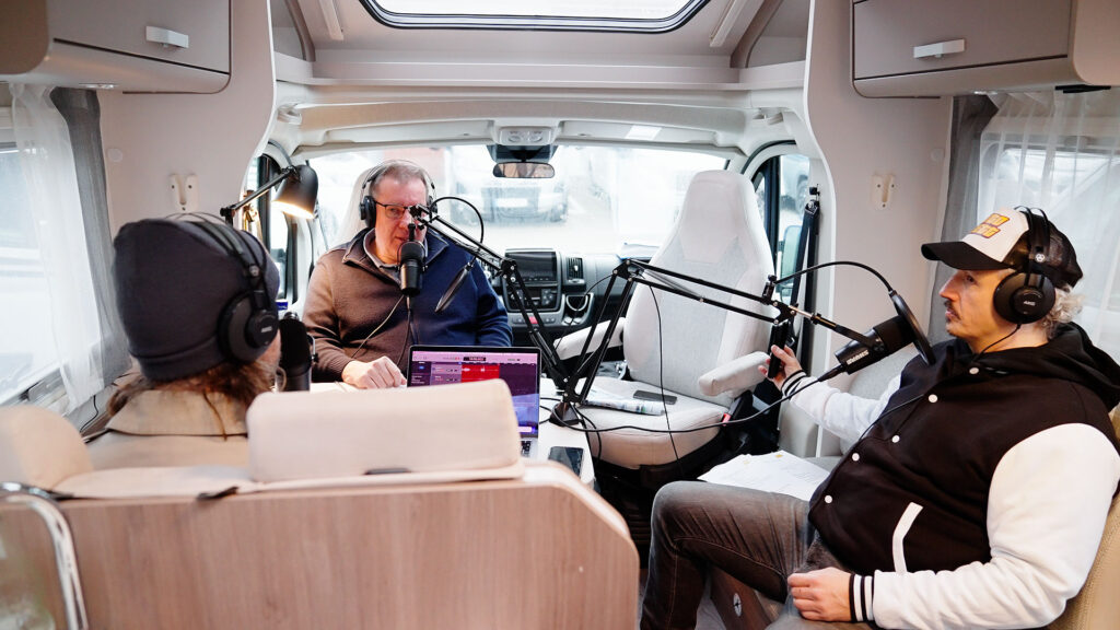 Drei Männer nehmen in lockerer Stimmung einen Podcast in einem hellen Wohnmobil auf