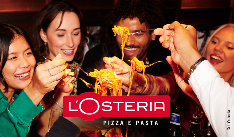 Vier fröhliche junge Erwachsene genießen gemeinsam bunte Pasta in lebhafter Runde