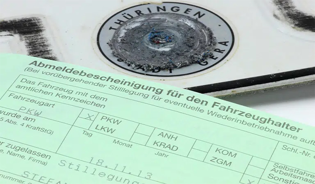 Ein entwertetes Nummernschild aus Thüringen liegt hinter einem grünen Abmeldeschein