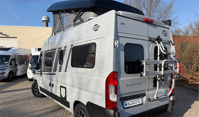 Grauer Campervan mit offenem Dachfenster, Fahrradträger und auffälligen Streifen