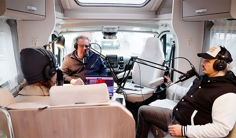 Drei Männer nehmen entspannt einen Podcast in einem weißen Wohnmobil auf