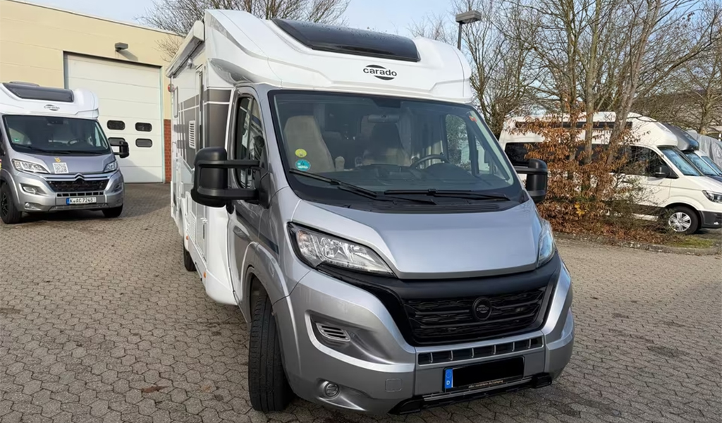 Grauer Wohnmobil Van mit schwarzen Spiegeln und großen Fenstern auf einem Parkplatz