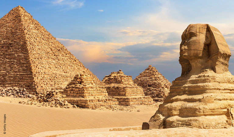 Bunte Häuser und eine grüne Kirche mit Turm stehen unter blauem Wolkenhimmel