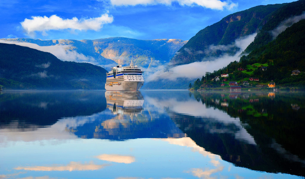 Ein roter Leuchtturm steht auf einer grünen Düne an einem ruhigen Sandstrand