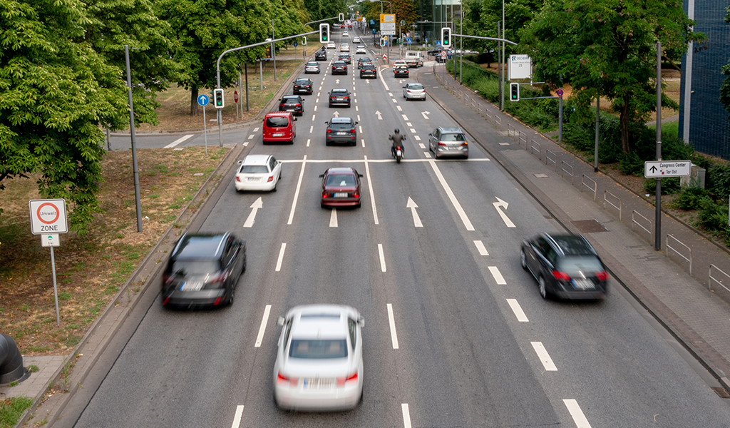 Mehrspurige Straße mit verschiedenen Autos und einem Motorrad an einer grünen Ampel