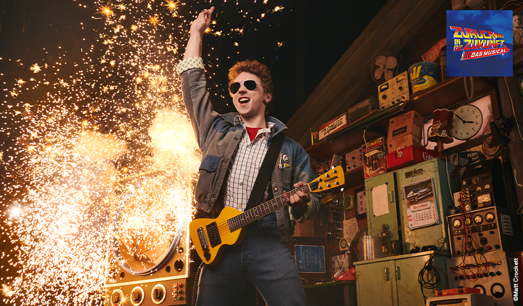 Ein junger Mann mit lockigem Haar spielt begeistert E-Gitarre vor Funkenregen in einer Werkstatt